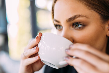 Portrait of young woman drinking coffee at table in cafe