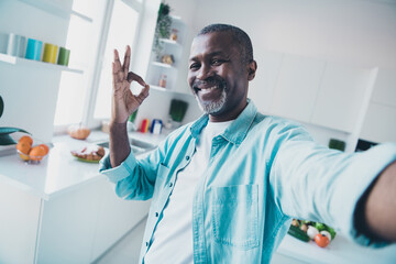 Photo of positive aged man make selfie okay symbol advise good apartment property in modern house kitchen