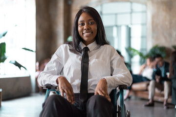 Portrait of a girl with a disability in a wheelchair smiling in her office lobby - young African American with walking difficulties smiles looking at camera - Powered by Adobe