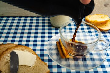 person serving traditional brazilian coffee in a cup. table set with toast, bread, cottage cheese and milk