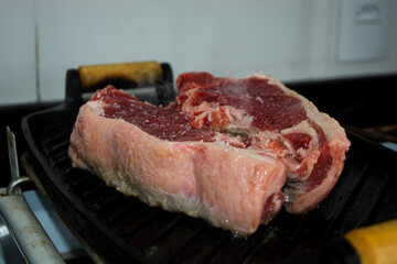 red raw sirloin steak being grilled on iron cast during day-time family lunch on a weekend