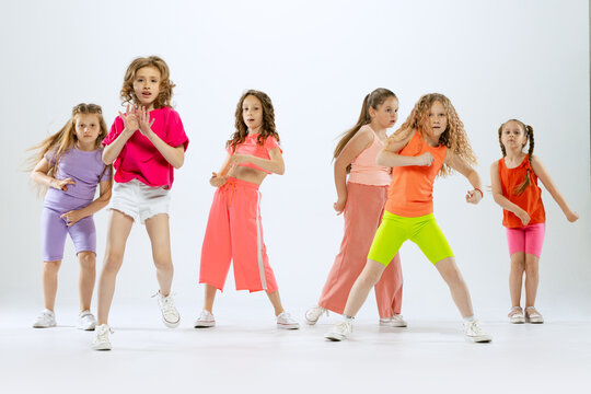 Portrait of happy, active little girls, happy kids in bright colorful clothes dancing isolated on white studio background. Concept of music, fashion, art, childhood, hobby