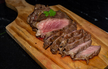 rare sirloin steak grilled, on wooden cutting board and black surface