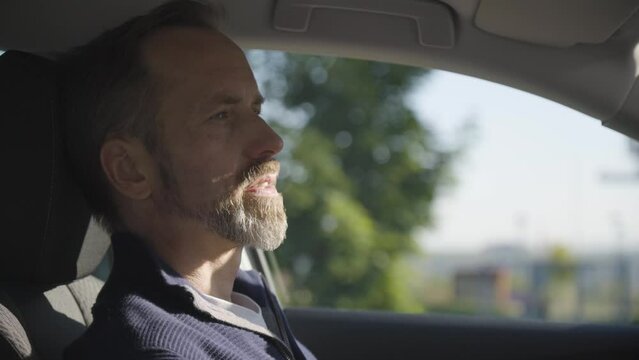 A middle-aged handsome Caucasian man waits, relaxes and thinks in a car - side closeup