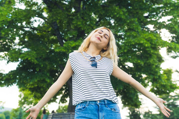 medium shot of a cute blond Caucasian girl standing with hands outstretched and enjoying the fresh air in the park. High quality photo