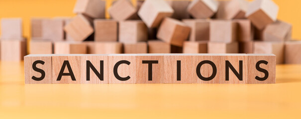 Text SANCTIONS on wooden cubes. Yellow background with heap bloks.