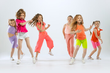 Happy, sportive little girls, kids in bright colorful clothes dancing modern dance isolated on...