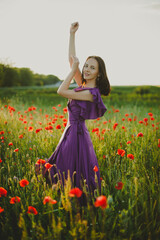 Obraz na płótnie Canvas Girl at blooming poppy field. Young woman posing in poppy field in evening time 
