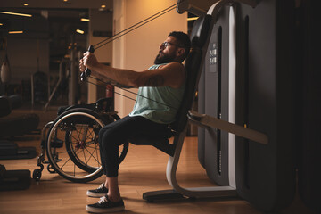 A middle-aged person in a wheelchair training in a gym. Working the pecs. Sports overcoming concept.