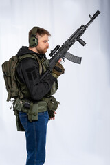 airsoft player in full gear with weapons series GG RK74 fire. a man in an outfit, in headphones, a bulletproof vest, with a backpack and a belt. White background.