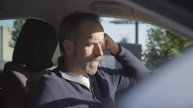 A middle-aged handsome Caucasian man talks to the camera in a car - closeup