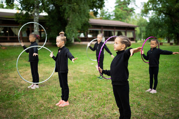 Group of girls trainees doing exercise with hoop on rhythmic gymnastics training outdoors in sports...