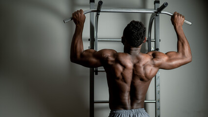 African american man with naked torso pulls up on horizontal bar in gym. 