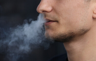 close up of a man with an electronic cigarette. man smokes an electronic cigarette in a natural...