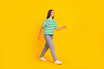 Full length profile photo of cheerful nice girl walking look empty space isolated on yellow color...