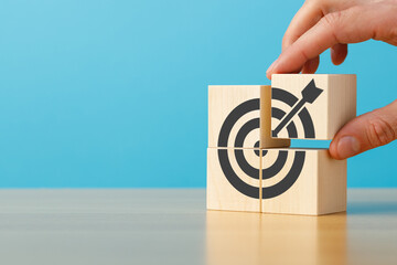 Male hand putting stack of wooden blocks with target icon on wooden table blue background copy...