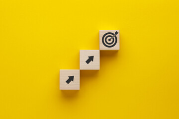Wooden cubes with arrows and target icons on yellow background. Business development strategy, advancement and goal concept.