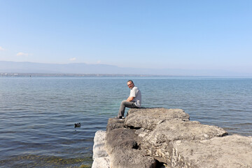 Fototapeta na wymiar A charming man about 40 years old, sitting on rocks staring out to the lake