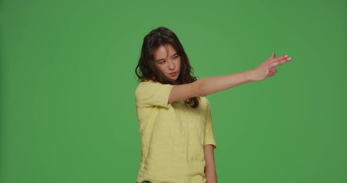 Cool young girl make gun gesture, searching for target shooting with hand pistol to camera on chromakey green background