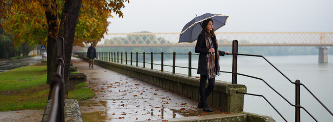 Beautiful girl with umbrella walking outdoor on a rainy misty autumn day