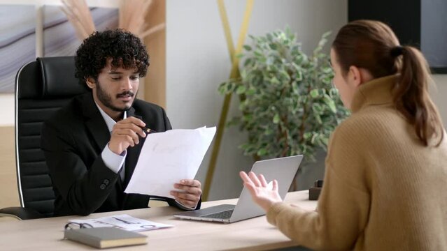 Serious successful Indian HR manager, entrepreneur, interviewing girl in modern office. Conversation of two colleagues, business partners discussing financial report, business strategy, business plan