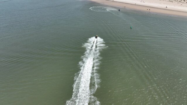 An aerial view over Gravesend Bay in Brooklyn, NY as a jet skier enjoys the beautiful day. The drone camera tilted down, dolly in then tilt up to follow the speeding jet skier as he heads to shore.