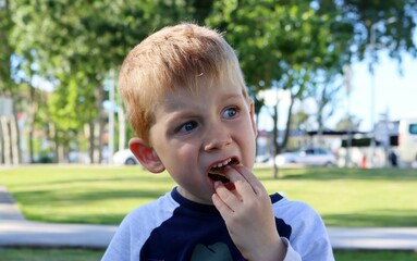 Fototapeta premium The blond boy opens his mouth and puts chips in it. A five-year-old boy eats junk food greedily. 