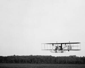 Wright Brothers tweedekker type B vliegt over een veld met bomenbossen op de achtergrond. Wright Brothers-vliegtuig wordt getest. Eerste militair vliegtuig gekocht door de VS. Tweedekker circa 1910 kopie ruimte