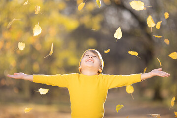 Happy child throw up yellow leaves outdoor in autumn park