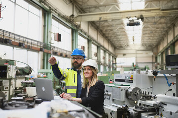 Male and female industrial engineers discussing factory's new machinery project and using laptop.