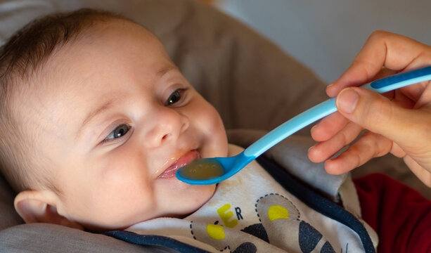 Close-up of a few months old baby starting weaning by eating a fruit puree.