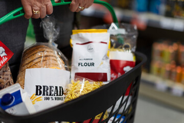 Woman shopping at the supermarket, she is carrying full shopping basket, close-up.
