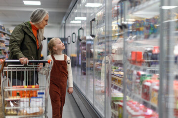 Grandmother with her granddaughter buying food in supermarket.