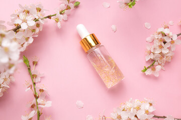 Glass bottle with oil, serum on a pink background with blooming cherry. Flat lay, minimalism....
