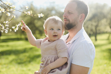 Fototapeta premium father and his adorable toddler daughter having fun in blossoming garden on beautiful spring day