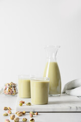 Pistachio nutty milk in glasses and pistachios on white background. Vegan lactose free milk replacer. Vertical. Close up.