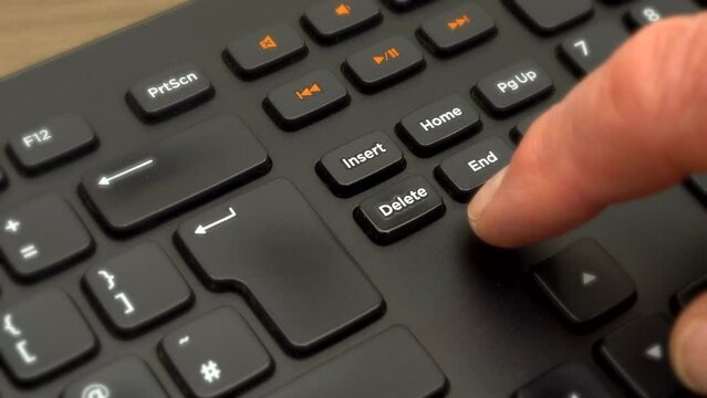 Closeup of a finger slowly pressing the Delete key four times in succession on a computer keyboard.