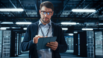 Male IT Specialist Walks Between Row of Operational Server Racks in Data Center. Engineer Uses...
