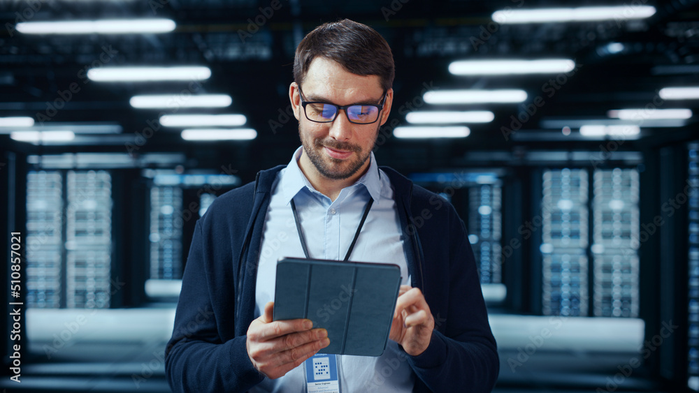 Poster Portrait of a Bearded Handsome Caucasian IT Specialist in Glasses Standing with Tablet and Posing in the Middle of a Working Data Center Server Room with Server Computers Working on a Rack.