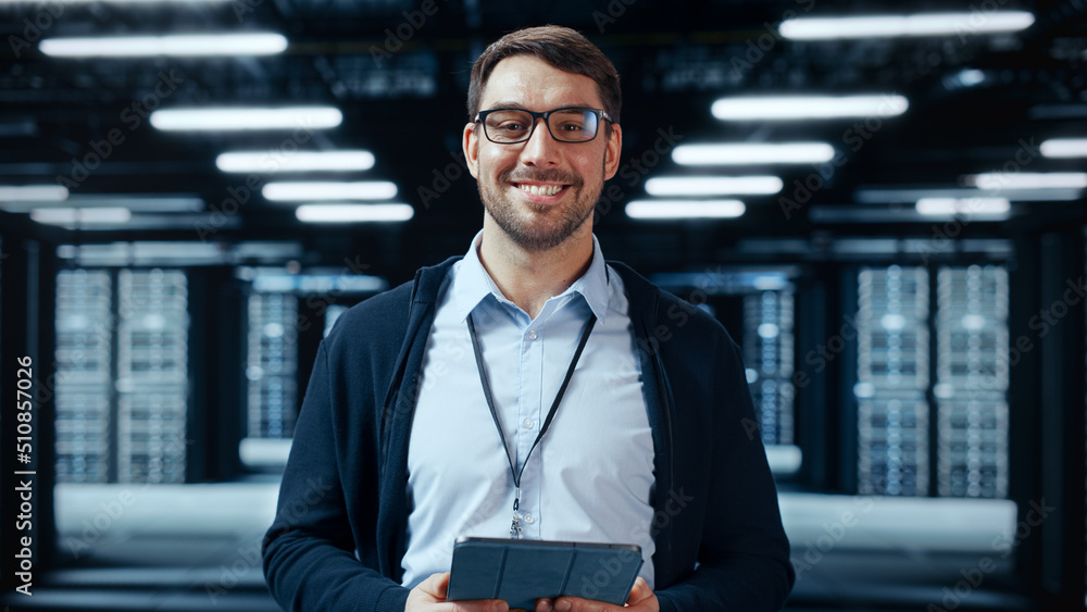 Poster Portrait of a Bearded Handsome Caucasian IT Specialist in Glasses Standing with Tablet and Posing in the Middle of a Working Data Center Server Room with Server Computers Working on a Rack.