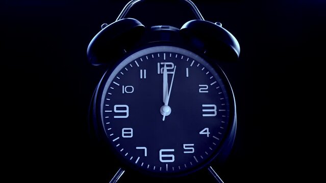 Closeup isolated shot on a dark background of a traditional analog alarm clock face, in dark blue color, with its bells ringing as the time pointers reach 12 o&rsquo;clock.