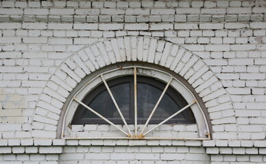 A semicircular barred window in a white brick wall