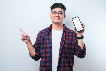 Young handsome asian man showing blank screen of smartphone very happy pointing with hand and finger to the side