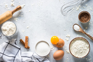 Baking background ingredients. Flour, sugar, eggs and rolling pin at light stone table. Top view...
