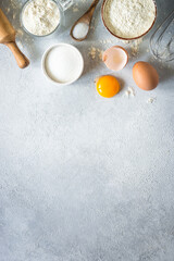 Baking background ingredients. Flour, sugar, eggs and others at light stone table. Top view with...