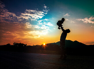 silhouette of  father holding baby at sunset