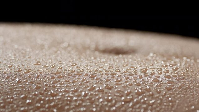 Macro shot of a lot of water drops on moving belly of young African American slim woman on black background | Skin texture shot for moisturizer commercial