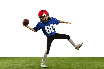 Fototapeta na wymiar Sportive little boy in sports uniform and equipment playing american football isolated on white background with green grass flooring. Concept of sport, movement, achievements.