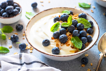 Greek Yogurt with granola and blueberies at light kitchen table.