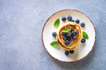 Pancakes stack with fresh blueberries and honey at stone table. Healthy breakfast or dessert. Top view with copy space.
